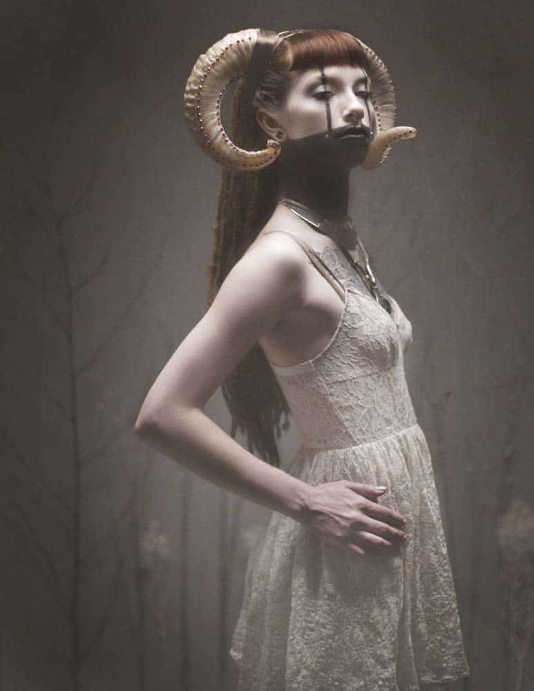 Egan is wearing ram horns and a white dress personifying Aries in this Gothesque editorial portrait