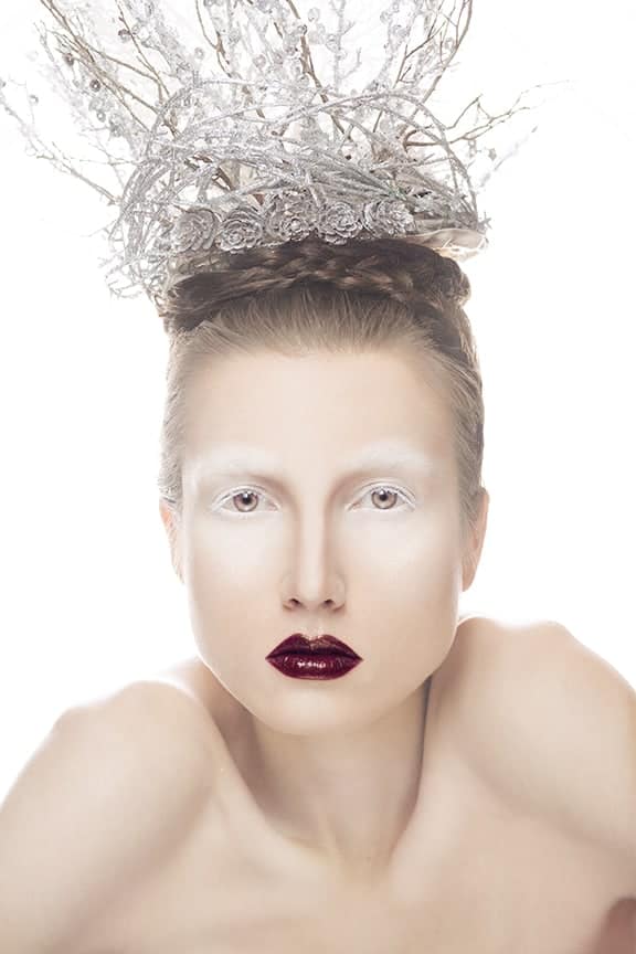 Melanie wears a brilliant silver crown of twigs with intense white eyeshadow, her eyes a golden brown, and a juicy burgundy lip