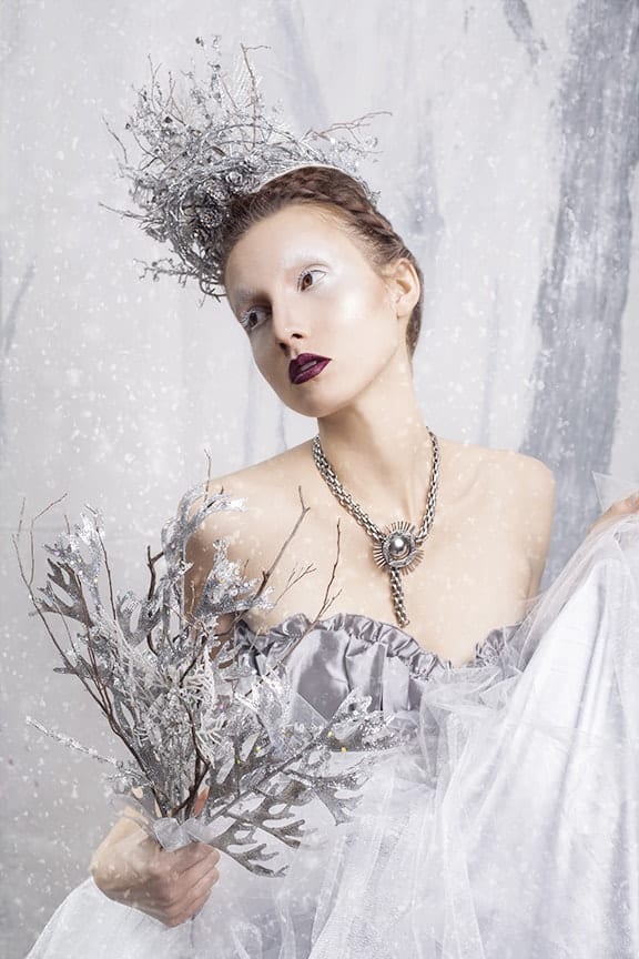 Her crown and scepter of silver twigs, Melanie stands against a winter backdrop in falling snow